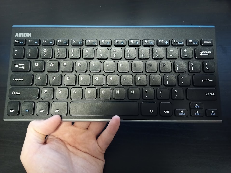 A hand holding a compact keyboard over a desk.