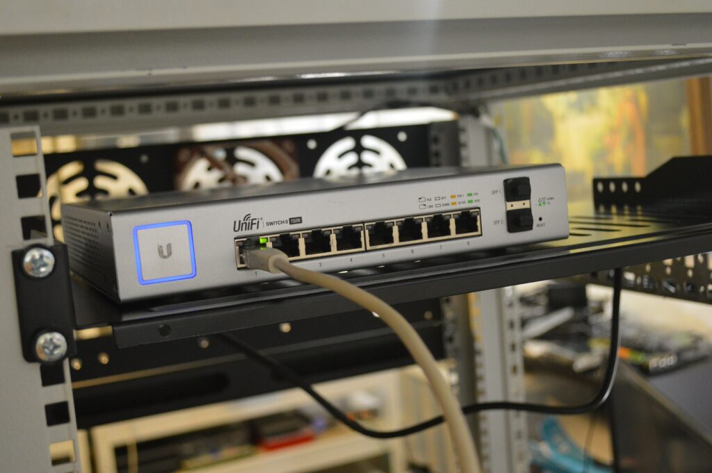 A network switch on a shelf with a yellow cable connected to the leftmost port.