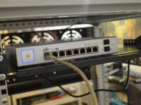 A network switch on a shelf with a yellow cable connected to the leftmost port.